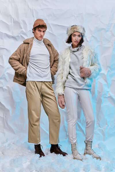 зимняя модная книга, межрасовая пара в теплой повседневной одежде позирует на белом снегу в студии