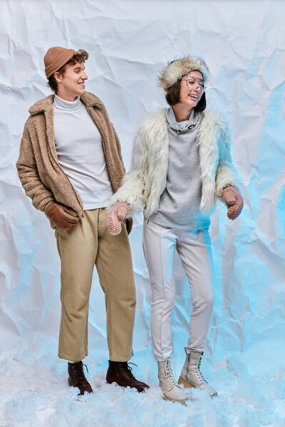 модная многонациональная пара в холодную погоду, смеющаяся над снегом в студии, зимнее счастье
