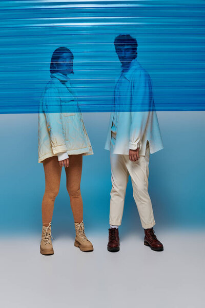 full length of interracial couple in leather boots behind blue plastic sheet in studio, winter trend