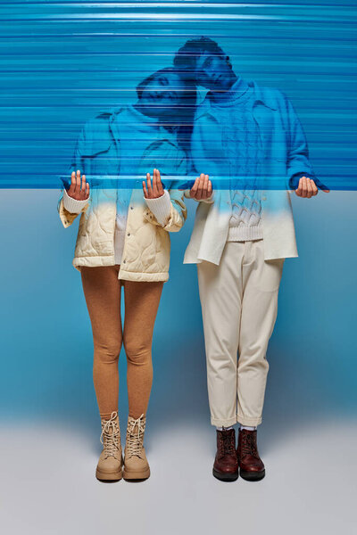 interracial couple in leather boots holding blue plastic sheet in studio, winter fashion concept