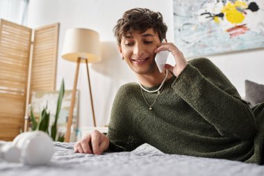 Mutlu ve kıvırcık kıvırcık giyinmiş biri yatak odasında akıllı telefondan konuşuyor, iletişim kuruyor.