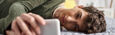 kıvırcık transseksüel blog yazarı akıllı telefon kullanıyor ve yatakta uzanıyor, sosyal medya etkili pankart