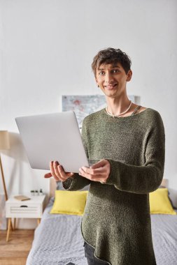 transgender blogger with curly hair using laptop while standing in modern apartment, influencer clipart