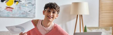 happy androgynous freelancer in pink sweater and eyeglasses working remotely, paperwork banner clipart