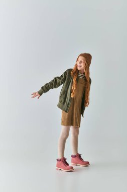 Kış kıyafetli ve örgü şapkalı neşeli bir kız. Gri ellerle poz veriyor.