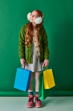 black friday and holiday season, dreamy girl in winter outfit and ear muffs holding shopping bags clipart