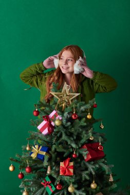 Tatiller, kulaklık takan neşeli bir kız ve turkuazda süslü Noel ağacının arkasında duruyor.