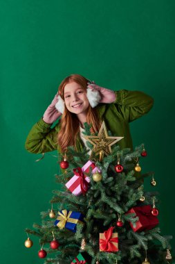 Noel ruhu, kulaklık takan mutlu bir kız ve turkuazda süslü Noel ağacının yanında duruyor.