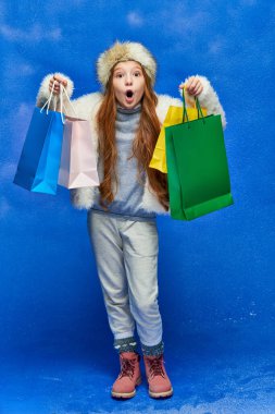 holiday shopping, shocked girl in faux fur jacket and hat holding shopping bags on turquoise, snow clipart