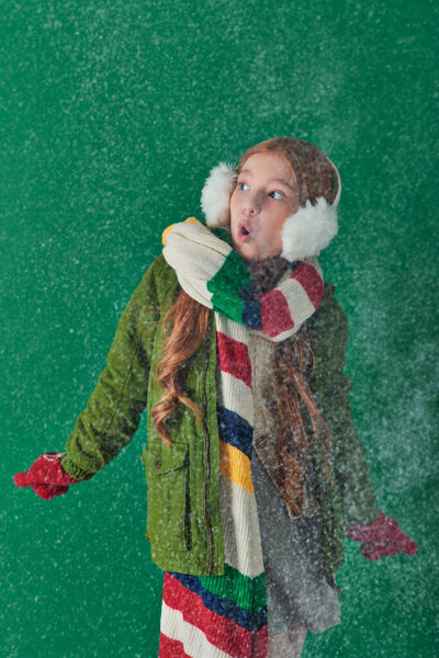 шокированная девушка в наушниках, полосатый шарф и зимний наряд стоя под падающим снегом на бирюзовой