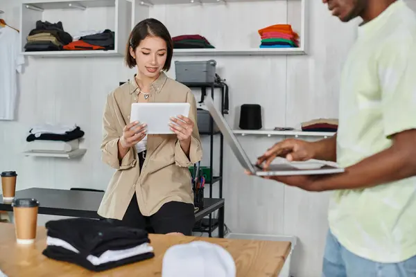 stock image smiling asian designer with digital tablet near african american man with laptop in print studio