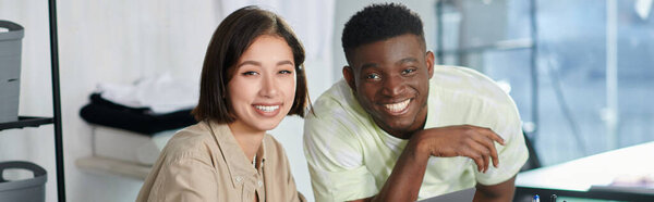 successful multiethnic fashion designers smiling at camera in print studio, horizontal banner
