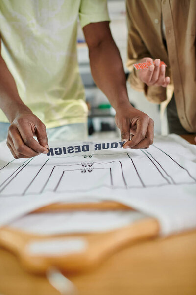 cropped view of interracial fashion designers holding text templates near t-shirt with format sizes
