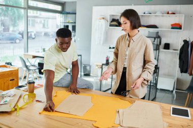 young multicultural clothes designers working with sewing patterns in professional print studio clipart