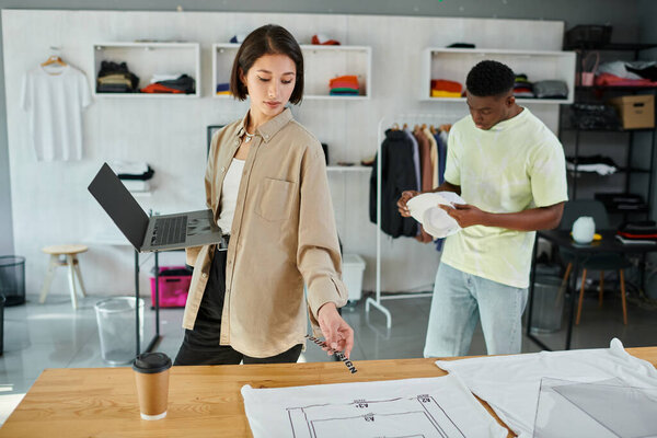 asian designer with laptop and text template near clothes and african american man in print studio