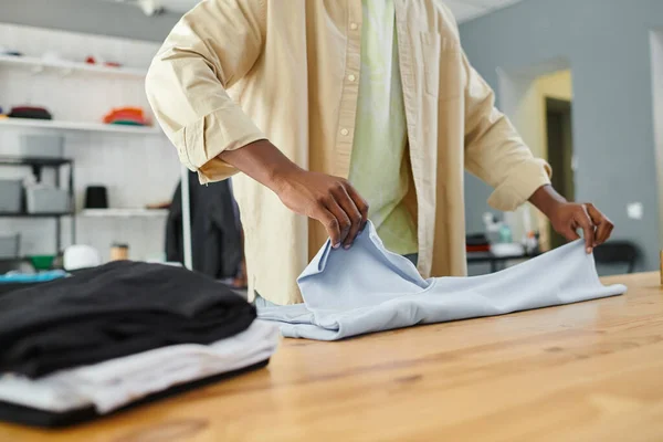 partial view of diligent skilled african american worker of print studio folding clothing on table