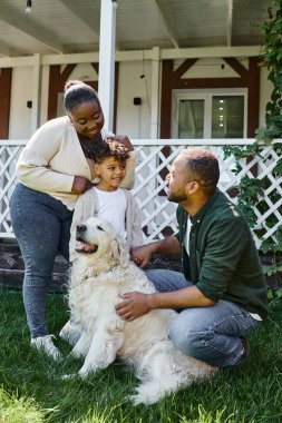 Neşeli Afro-Amerikan ailesi evlerinin arka bahçesinde köpekle oynuyor.