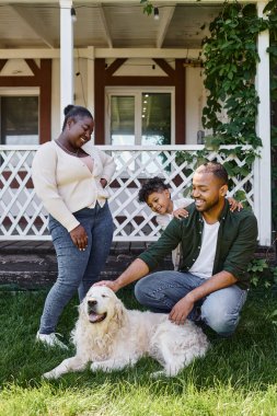 Neşeli Afro-Amerikan ailesi evlerinin arka bahçesinde köpekle oynuyor.