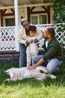 Neşeli Afro-Amerikan ebeveynler ve oğulları evlerinin arka bahçesinde köpekle oynuyorlar.