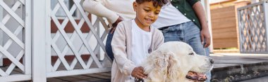 Pozitif Afro-Amerikalı çocuk evinin arka bahçesinde ailesinin yanında köpekle oynuyor.
