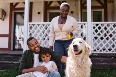 Modern ebeveynlik, mutlu Afro-Amerikan baba ve oğlu arka bahçede kadın ve köpeğin yanında oynuyorlar.