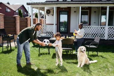 Aile hafta sonu, mutlu Afro-Amerikan babası, karısının yanındaki oğluna futbol topu veriyor, sofra kuruyor.
