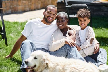 Afro-Amerikan ailesinin aile portresi. Kameraya bakıyor ve köpek yakınındaki çimlerde oturuyor.