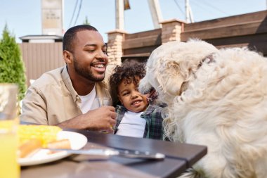 Mutlu Afro-Amerikan babası ve kıvırcık oğlu arka bahçede aile bbq sırasında evcil köpek, aile