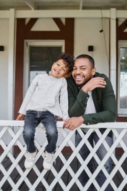 Pozitif Afro-Amerikan baba ve oğlu gülümsüyor ve verandada oturuyor, aile portresi