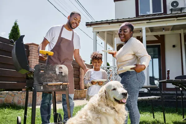 幸せなアフリカ系アメリカ人男性は 裏庭に犬 息子の近くのBbqグリルでグリルトウモロコシを準備 — ストック写真