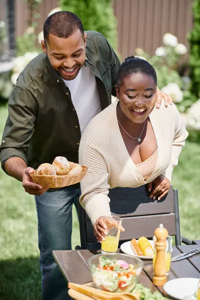幸せなアフリカ系アメリカ人は 庭でテーブルを提供する夫婦 パンとオレンジジュースのガラス — ストック写真