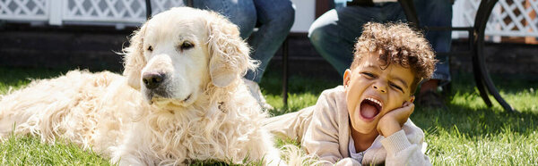 emotional african american boy lying on green lawn next to family dog on backyard, horizontal banner