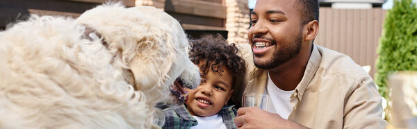 happy african american father and curly son petting dog on backyard of house, horizontal banner