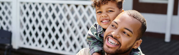 positive african american boy hugging excited father in braces on backyard of house, banner