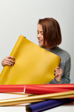 Gri arka planda sarı hediye kağıdı tutan süveterli genç bir kadın. Mutlu Noeller konsepti.