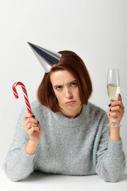 Parti şapkalı hoşnutsuz kadın elinde şampanya bardağı ve şeker kamışı tutuyordu gri, mutlu Noeller