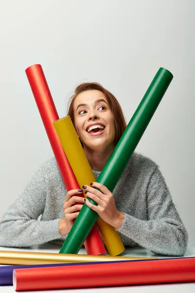 stock image woman in winter sweater holding colorful wrapping paper and dreaming on grey backdrop, Christmas