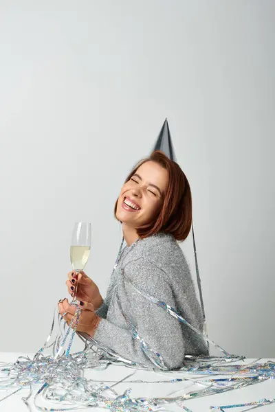 cheerful woman in party cap and tinsel on head holding champagne glass while celebrating New year