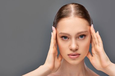 portrait of beautiful young woman with perfect skin posing with hands near face on grey background clipart