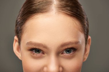 cropped view of young woman with blue eyes and perfect skin looking at camera on grey background clipart