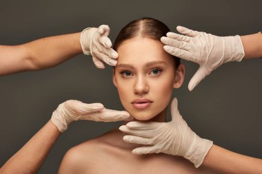 estheticians in medical gloves examining face of young woman on grey background, facial treatment clipart