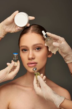estheticians in medical gloves holding different beauty treatment products near young woman on grey clipart