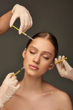 estheticians in medical gloves holding syringes near young woman on grey background, rejuvenation clipart