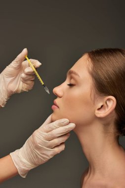 esthetician in medical glove holding syringe near lips of young woman on grey background, filler clipart