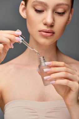 Parlak derili genç bir kadın elinde serum şişesiyle gri arka planda, su kaybına uğramış.
