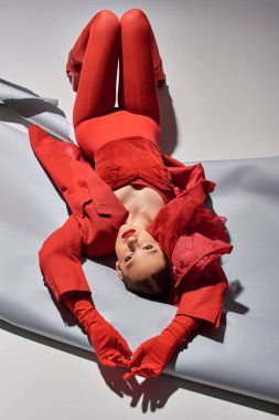 Gri arka planda duran kırmızı elbiseli tam boy genç manken, kameraya bakın.