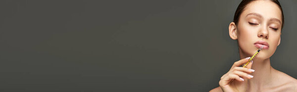 портрет молодой женщины, держащей шприц у лица на сером фоне, баннер для увеличения губ