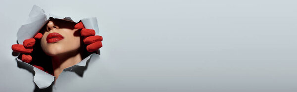 обрезанный баннер молодой женщины с красными губами в перчатках разорвать серый фон и сделать отверстие