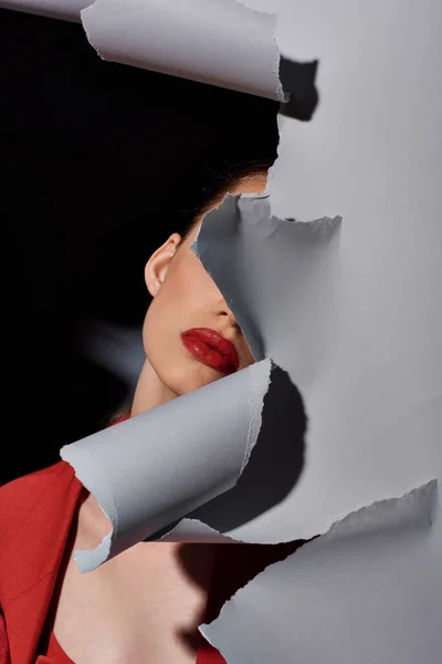 Stock image partial view of young woman with red lips posing near torn grey paper, bold makeup and fashion