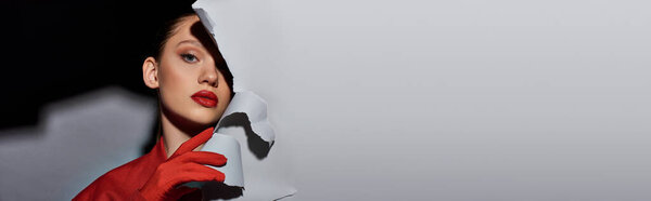 знамя красивой молодой женщины с ярко-красными губами, позирующими рядом с порванной серой бумагой и смотрящей в камеру